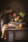 Unerkennbarer älterer Mann nimmt reife Früchte aus Metallkorb auf rustikalem Tisch — Stockfoto