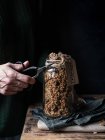 Pessoa irreconhecível usando tesoura retro para cortar corda com etiqueta de frasco de vidro de milho e quinoa granola — Fotografia de Stock