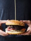 Обрізати анонімну особу в чорному одязі, тримаючи класичний бургер з котлети та овочі з сиром, представляючи індустрію фаст-фуду — стокове фото