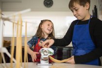 Ein kleines Mädchen mit älterem Bruder mit Nudelmaschine bei der Zubereitung hausgemachter Nudeln in der heimischen Küche — Stockfoto