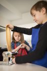A little girl with older brother using pasta machine while preparing homemade noodles in home kitchen — Stock Photo