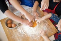 Niños preparando masa mientras están de pie juntos en la mesa de la cocina con harina - foto de stock