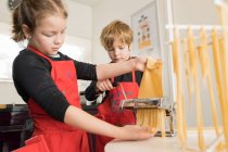 Маленька дівчинка з старшим братом використовує макаронні машини під час приготування домашньої локшини на домашній кухні — стокове фото