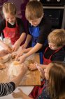 Kinder bereiten Teig zu, während sie gemeinsam am Küchentisch mit Mehl stehen — Stockfoto