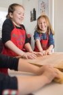 Симпатична маленька дівчинка в шеф-кухарі фартух замішує тісто на дерев'яному столі, вивчаючи рецепт домашньої локшини в кулінарному класі з дітьми — стокове фото