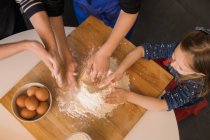 Les enfants préparent la pâte tout en se tenant ensemble à la table de cuisine avec de la farine — Photo de stock