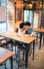 De cima animado homens étnicos abraçando e beijando uns aos outros na mesa e rindo durante a data romântica na cafetaria moderna — Fotografia de Stock