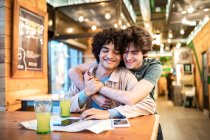 Giovani omosessuali multietnici che si abbracciano guardando la mappa di navigazione direzione e avendo bevande fresche sorridenti mentre si siede al tavolo del caffè durante appuntamento romantico — Foto stock