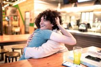 Emozionati uomini etnici che si abbracciano a occhi chiusi sul tavolo e ridono durante un appuntamento romantico nella moderna caffetteria — Foto stock