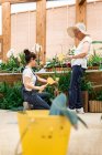 Взрослая женщина и пожилая женщина ставят желтую этикетку в горшки с растениями во время работы в теплице — стоковое фото