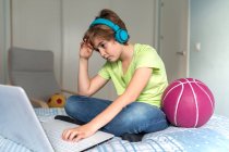 Serious schoolboy in casual outfit and headphones playing video game on laptop at home — Stock Photo