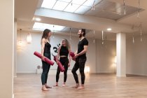 Young man and women with mats speaking with each other while standing in spacious studio during yoga training — Stock Photo