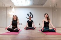 Calmo relaxante mulheres e homem com os olhos fechados sentado em pose de lótus com as mãos mudra concentradas depois na aula de ioga — Fotografia de Stock