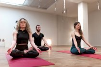 Calmo relaxante mulheres e homem com os olhos fechados sentado em pose de lótus com as mãos mudra concentradas depois na aula de ioga — Fotografia de Stock