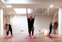 Ausgeglichene, ruhige Frauen und Männer, die sich auf Dehnung und Heben der Hände in Kriegerhaltung und ausgedehnter Seitenwinkelhaltung im Yoga-Kurs konzentrieren — Stockfoto