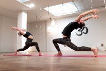 Vista lateral de mujer tranquila equilibrada y hombre concentrado en estirar y levantar las manos en guerrero una postura en clase de yoga - foto de stock
