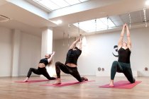 Vista laterale di donne calme equilibrate e uomo concentrato su stretching e alzando le mani in guerriero una postura sulla classe di yoga — Foto stock