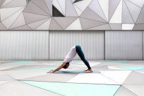 Seitenansicht eines erwachsenen Männchens in Sportbekleidung, das im geräumigen Raum beim Yoga gegen eine geometrische Wand hetzt — Stockfoto