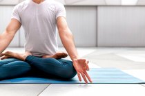 Cropped unrecognizable man in sportswear sitting in Lotus pose and meditating with closed eyes and mudra gesture in spacious room with geometric wall and floor — Stock Photo