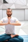 Дорослий бородатий чоловік у спортивному одязі сидить схрещеними ногами і роздумує із закритими очима і застібнутими руками під час тренування йоги в геометричній кімнаті — стокове фото