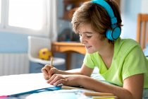 Seitenansicht positiver Schüler in Freizeitkleidung und drahtlosem Kopfhörer, der mit Bleistiften zeichnet, während er seine Freizeit im Schlafzimmer verbringt — Stockfoto