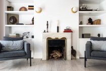Комфортні сірі сидіння, розташовані біля каміна і книжкової полиці в затишній вітальні в стильній квартирі — стокове фото