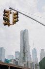 Desde debajo del semáforo colgando sobre la carretera en la ciudad de Nueva York con rascacielos contemporáneos y cielo nublado en el fondo - foto de stock