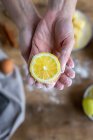 De arriba la mano de la cosecha de la mujer irreconocible cubierta de la harina que sostiene y que muestra a la cámara un limón fresco medio cortado - foto de stock