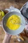 From above top view of crop anonymous woman whipping eggs in black bowl on wooden table with lemon , flour, butter and cinnamon sticks ingredients for cake — Stock Photo