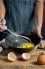 Ernte anonyme Frau in Schürze schlagen Eier in schwarzer Schüssel auf Holztisch mit Zitrone, Mehl, Butter und Zimtstangen Zutaten für Kuchen — Stockfoto