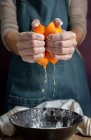 Обрізати руку невпізнаваної жінки в фартусі, стискаючи свіжий соковитий нарізаний апельсин над мискою, готуючи тісто за столом — стокове фото