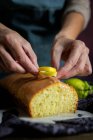 Обрезанные неузнаваемые женские руки готовят домашний вкусный лимонный торт, покрытый глазурью и ломтиками лимона — стоковое фото