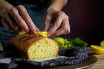 Zugeschnittene unkenntliche Frauenhände bereiten einen hausgemachten leckeren Zitronenkuchen mit Glasur und Zitronenscheiben zu — Stockfoto