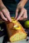 Зверху обрізані невпізнавані руки жінки готують домашній смачний лимонний торт, покритий глазур'ю та лимонними скибочками — стокове фото