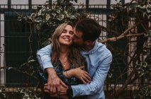 Content young man and woman hugging and kissing while standing near metal fence on city street and enjoying summer day together — Stock Photo