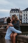 Felice giovane donna seduta sul vecchio recinto di pietra e abbracciare fidanzato affettuoso mentre trascorre la serata estiva insieme a Bayonne — Foto stock