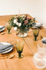 Buquê de flores diversas e ramos de plantas verdes em vaso com água em uma mesa de madeira para uma refeição — Fotografia de Stock