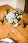 D'en haut bouquet de fleurs diverses et de brindilles de plantes vertes dans un vase avec de l'eau sur une table en bois pour un repas — Photo de stock