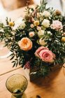 De haut bouquet de fleurs diverses et brindilles de plantes vertes dans une boîte en bois sur une table en bois pour un repas — Photo de stock