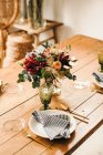 D'en haut bouquet de fleurs diverses et de brindilles de plantes vertes dans un vase avec de l'eau sur une table en bois pour un repas — Photo de stock