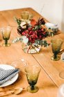 Von oben Bouquet von verschiedenen Blumen und grünen Pflanzenzweigen in der Vase mit Wasser auf einem Holztisch für eine Mahlzeit gedeckt — Stockfoto