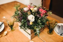 De haut bouquet de fleurs diverses et brindilles de plantes vertes dans une boîte en bois sur une table en bois pour un repas — Photo de stock