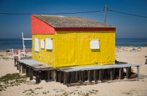 Небольшой разноцветный дом с обшарпанными стенами, расположенный на песчаном берегу с голубым небом на заднем плане в солнечный день — стоковое фото