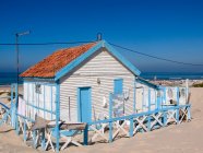 Kleine weiße und blaue Streifen Landhaus mit weißem Zaun am Meer gegen wolkenlosen blauen Himmel bei sonnigem Tag — Stockfoto