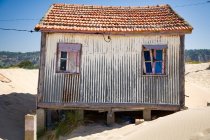 Pequena casa com paredes rasgadas localizadas à beira-mar arenoso com céu azul no fundo no dia ensolarado — Fotografia de Stock