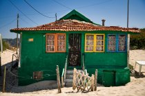Маленький будинок з бурхливими зеленими стінами і барвистими вікнами, розташованими на піщаному узбережжі з блакитним небом на фоні сонячного дня — стокове фото