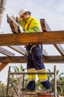 D'en bas du technicien masculin dans l'usure de travail debout sur l'échafaudage et la préparation de l'installation du panneau solaire sur la construction en bois — Photo de stock