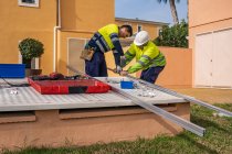 Group of male technicians in uniform working with alternative solar panels and preparing for installation near residential building — Stock Photo
