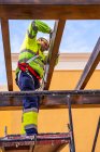Von unten Seitenansicht eines männlichen Technikers in Arbeitskleidung, der auf einem Gerüst steht und sich auf die Installation von Solarzellen auf Holzkonstruktion vorbereitet — Stockfoto