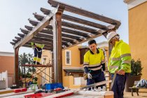 Группа техников-мужчин в форме, работающих с альтернативными солнечными панелями и готовящихся к установке возле жилого дома — стоковое фото
